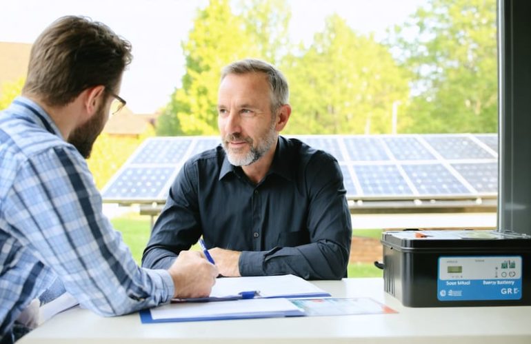 Homeowner consulting with insurance agent about solar battery coverage, with a solar battery system visible in the background.