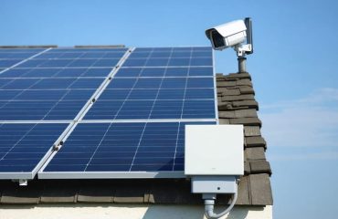 Rooftop solar panels equipped with security camera and anti-theft hardware under a clear sky, representing protection and renewable energy.