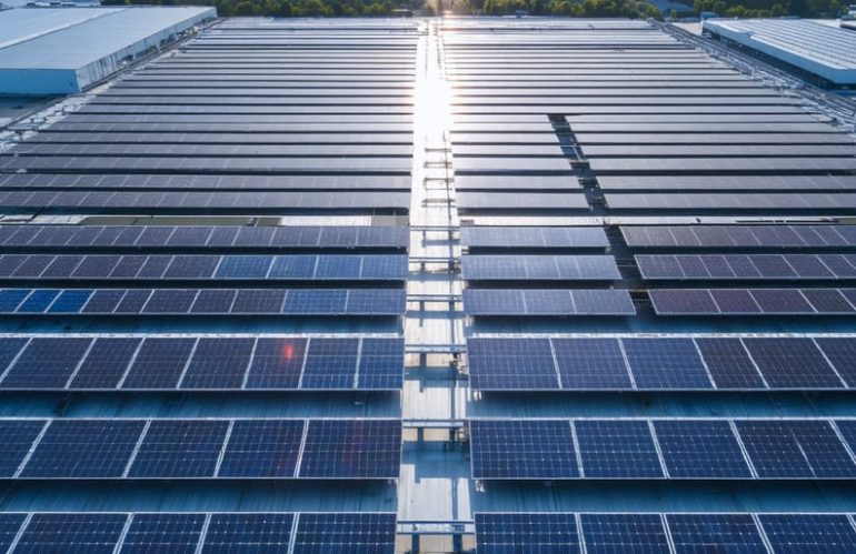 Aerial view of an industrial facility with extensive rooftop solar panel installation, representing the shift towards sustainable and cost-effective energy solutions for major corporations.