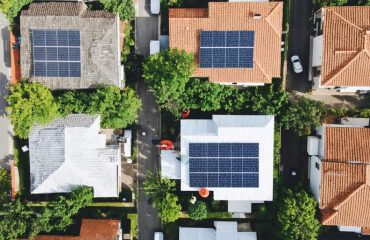 Aerial view of a neighborhood with houses featuring solar panels, surrounded by community members discussing solar initiatives, symbolizing collective energy solutions.