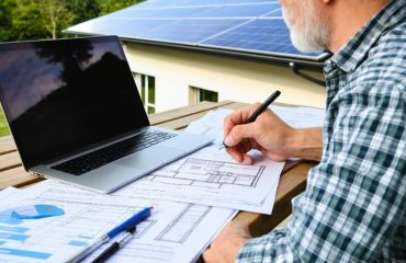 Homeowner reviewing solar panel installation plans and permits, with rooftop solar panels visible in the background, highlighting legal requirements and planning.