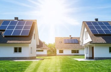 Suburban neighborhood with multiple homes featuring solar panels on rooftops under a bright and clear sky, illustrating solar energy's economic impact.