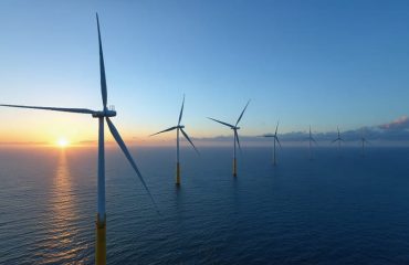 A panoramic view of a sprawling offshore wind farm at sunset, showcasing numerous towering wind turbines in the ocean, illustrating the transformative potential of offshore wind energy for achieving energy independence.