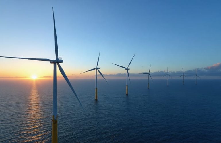 A panoramic view of a sprawling offshore wind farm at sunset, showcasing numerous towering wind turbines in the ocean, illustrating the transformative potential of offshore wind energy for achieving energy independence.
