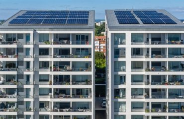 Modern apartment building showcasing innovative solar panel integrations, including balcony and window-mounted panels, with a shared community solar array in the background.