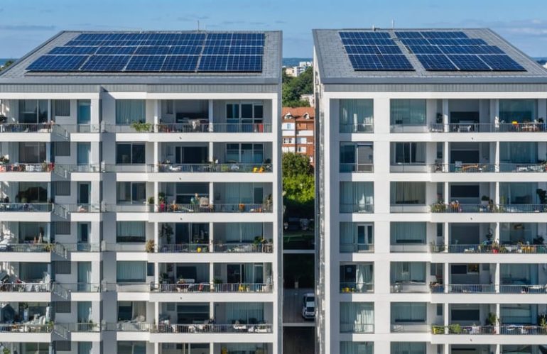 Modern apartment building showcasing innovative solar panel integrations, including balcony and window-mounted panels, with a shared community solar array in the background.