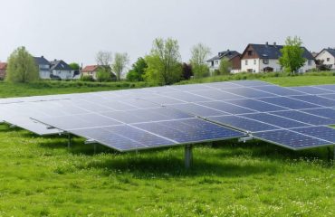 "Aerial view of a large solar panel array in a grassy field near a residential neighborhood."