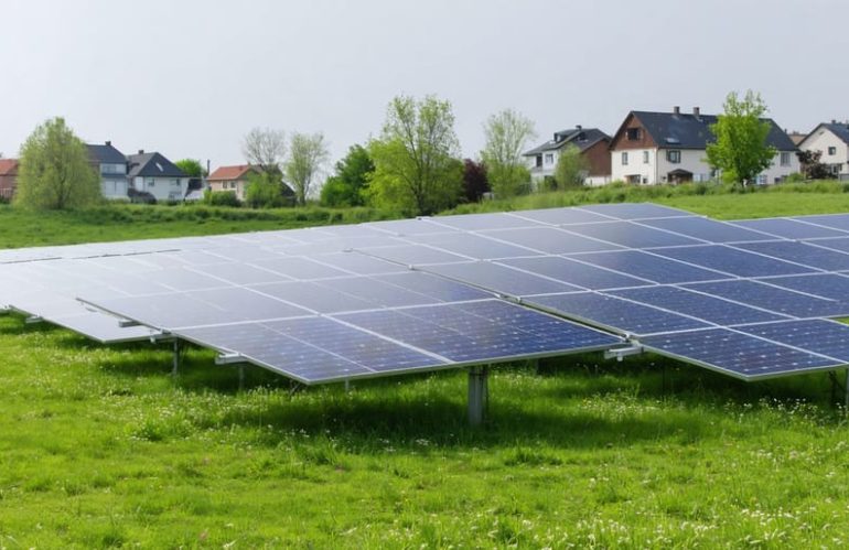 "Aerial view of a large solar panel array in a grassy field near a residential neighborhood."