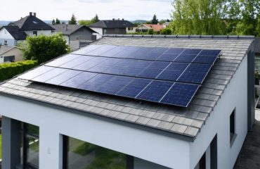 "Modern house with solar panels on the roof and a visible battery storage system, demonstrating sustainable energy technology."