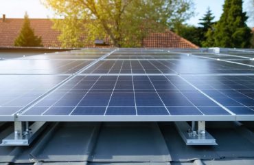 Low-angle photo of rooftop solar panels showing a clear ventilation gap under the array, lit by golden hour sunlight, with a softly blurred suburban neighborhood and open sky in the background.